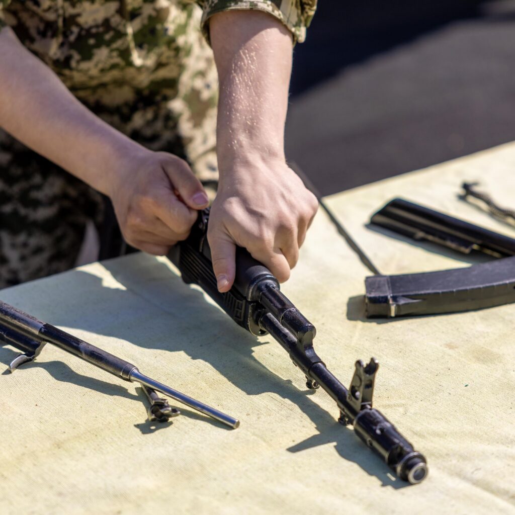 Close-up of a person assembling a rifle on an outdoor table during the day.