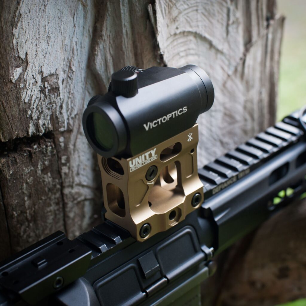 Close-up of a VictOptics gun sight mounted on a weapon outdoors with natural background.