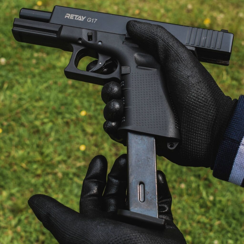Close-up of hands with gloves holding a disassembled firearm on grass.