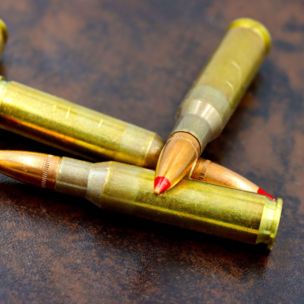 Detailed view of high-caliber rifle bullets with red tips on a textured surface.